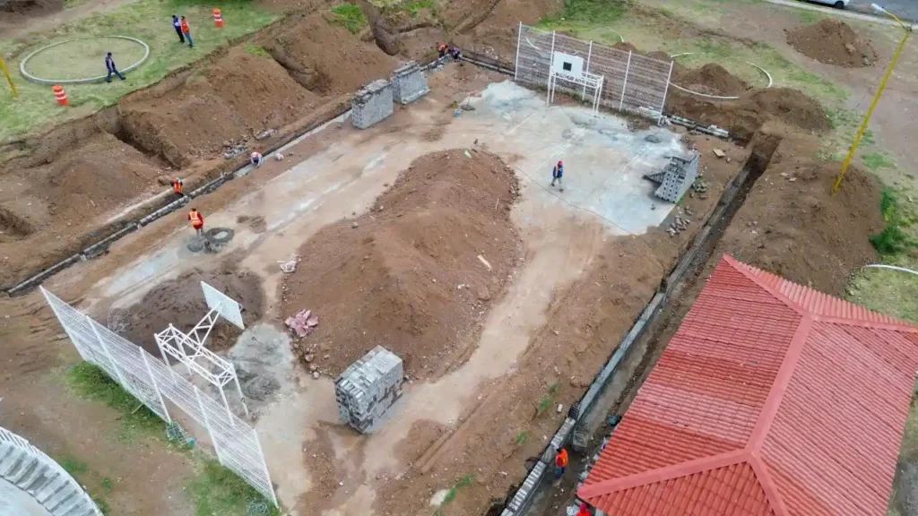 Vista aérea detallada de la cancha de usos múltiples y áreas perimetrales en etapa de nivelación y cimentación.