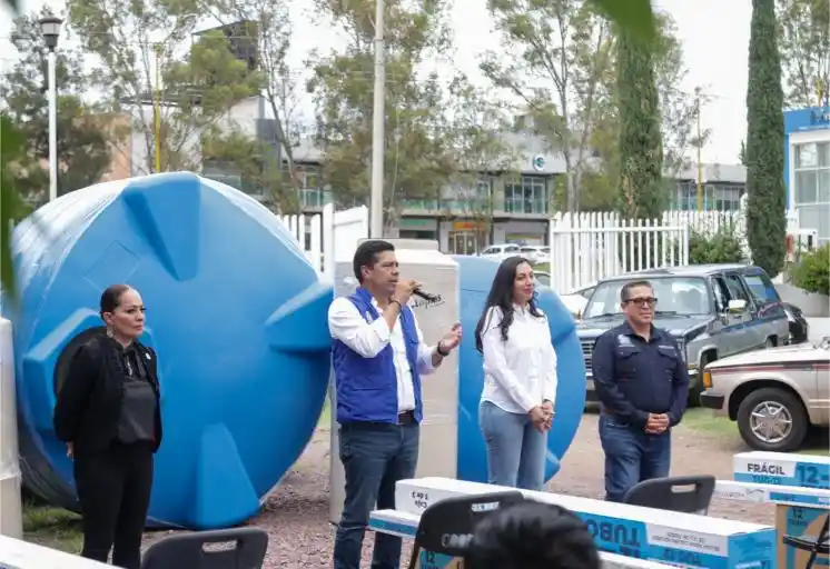 El alcalde Leo Montañez se dirige a las familias asistentes a la jornada de entrega de ecotecnias e insumos para la vivienda. Al fondo se aprecian tinacos de gran capacidad destinados al almacenamiento de agua potable.